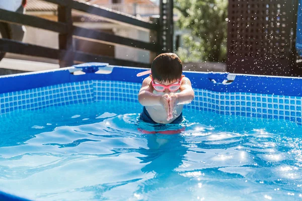 Child playing in a small removable pool of a house. Boy diving forward into the water with his hands, covering his nose with goggles. High quality photo