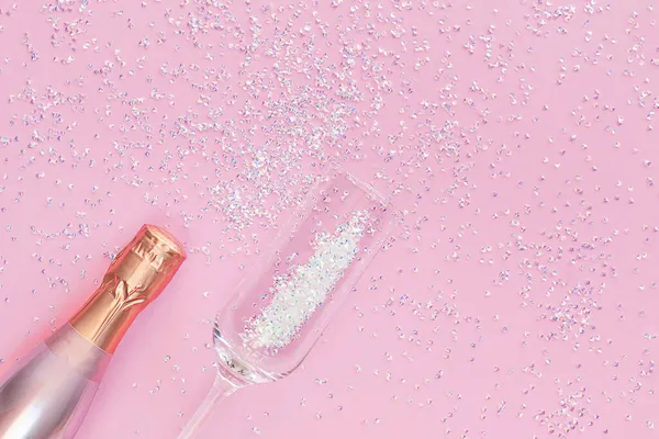 Une bouteille de champagne et un verre sur fond rose aux reflets argentés. — Photo