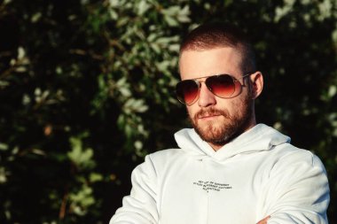 Kırsalda ya da parkta beyaz ceketli genç sakallı bir adamın portresi. Gündelik giysiler içindeki bir erkek geceyi doğada geçirir. Tarz kavramı, temiz havada yürümek ve doğayla birlik olmak.