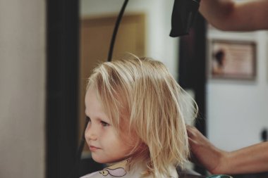 Berber kadın, modern berber dükkanında, kuaförde küçük sevimli sarışın kız çocuğu için şık bir saç stili yapıyor. Berber dükkanında kuaför, küçük bebek için kuaför yapar. Saç stili ve güzellik kavramı