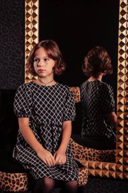 Hoş bir genç kızın portresi. Ayna karşısında zarif bir elbise içinde. Oturma odasının içinde. Çocuk duyguları ve poz verme. Tarz, moda ve güzellik kavramı. Alan için kopyala