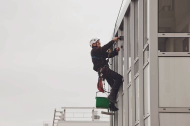 Endüstriyel dağcılık işçisi dış cephe camlarını yıkarken konut binasının ön cephesinde asılı duruyor. İp erişimi olan işçi ev duvarında asılı. Şehir işleri kavramı. Alan için kopyala