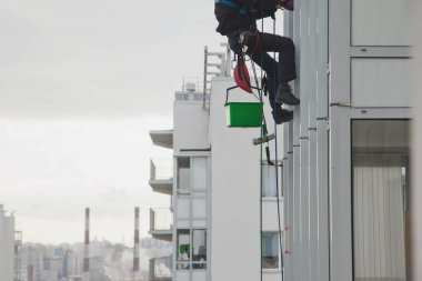 Endüstriyel dağcılık işçisi dış cephe camlarını yıkarken konut binasının ön cephesinde asılı duruyor. İp erişimi olan işçi ev duvarında asılı. Şehir işleri kavramı. Alan için kopyala