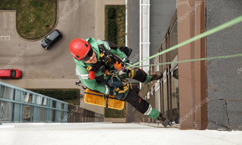 Industrial mountaineering worker hangs over residential facade building while washing exterior facade glazing. Rope access laborer hangs on wall of house. Concept of industry urban works. Copy space