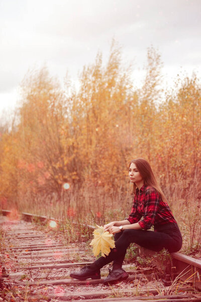 Portrait of cute young woman of Slavic appearance in casual wear in autumn, on railway road against background of an autumn Park and river. Pretty female walking in forest in golden fall. Copy space