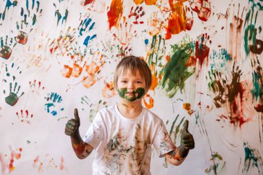 Suluboya ile oynayan mutlu genç bir çocuğun portresi. Çocuk yüzü ve kıyafetleri boyayla boyanmış. Çocuk eğlencesi, sanat oyunları ve holiganlığı kavramsallaştır. Holi festivali için renkli görüntü. Boşluğu kopyala