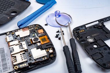 Masanın üzerinde bozuk bir akıllı telefon ve tamir aletleri var..