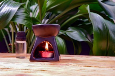 İçinde mum olan aromatik bir lamba, yeşil yapraklardan oluşan bir arka planda, ahşap bir masanın üzerinde duruyor..