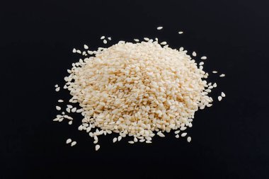 Siyah arka planda küçük bir susam tohumu yığını var.,