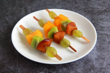 Taze meyvelerden yapılmış çocuk partisi için meyve kebabı. Taze kivi, erik, üzüm, ahşap çubuklarda hurma. Doğum günü partisi için egzotik meyve mezeleri..