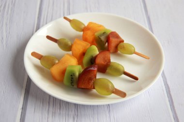 Taze meyvelerden yapılmış çocuk partisi için meyve kebabı. Taze kivi, erik, üzüm, ahşap çubuklarda hurma. Doğum günü partisi için egzotik meyve mezeleri..