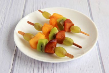 Taze meyvelerden yapılmış çocuk partisi için meyve kebabı. Taze kivi, erik, üzüm, ahşap çubuklarda hurma. Doğum günü partisi için egzotik meyve mezeleri..