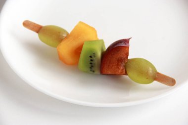 Taze meyvelerden yapılmış çocuk partisi için meyve kebabı. Taze kivi, erik, üzüm, ahşap çubuklarda hurma. Doğum günü partisi için egzotik meyve mezeleri..