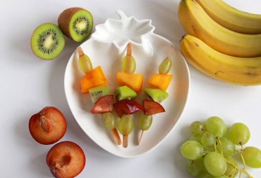 Taze meyvelerden yapılmış çocuk partisi için meyve kebabı. Taze kivi, erik, üzüm, ahşap çubuklarda hurma. Doğum günü partisi için egzotik meyve mezeleri..