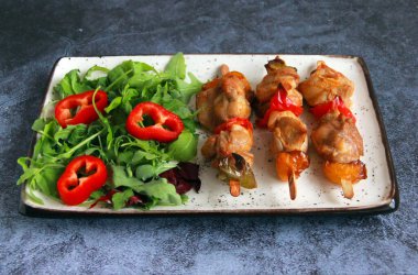 Tabaktaki tahta çubuklarda tavuk budu kebabı. Sıcak meze - kırmızı biberli tavuk şişi ve soğan ve taze sebze salatası.. 