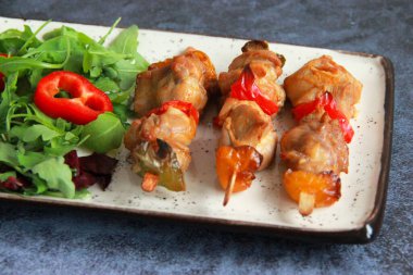 Tabaktaki tahta çubuklarda tavuk budu kebabı. Sıcak meze - kırmızı biberli tavuk şişi ve soğan ve taze sebze salatası.. 