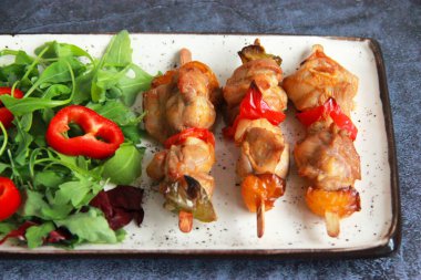 Tabaktaki tahta çubuklarda tavuk budu kebabı. Sıcak meze - kırmızı biberli tavuk şişi ve soğan ve taze sebze salatası.. 