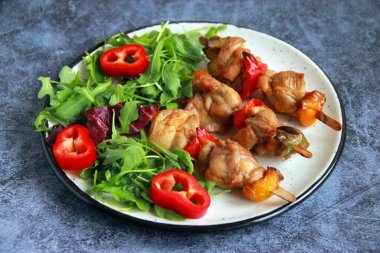 Tabaktaki tahta çubuklarda tavuk budu kebabı. Sıcak meze - kırmızı biberli tavuk şişi ve soğan ve taze sebze salatası.. 