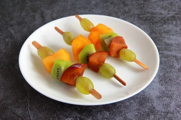 Taze meyvelerden yapılmış çocuk partisi için meyve kebabı. Taze kivi, erik, üzüm, ahşap çubuklarda hurma. Doğum günü partisi için egzotik meyve mezeleri..