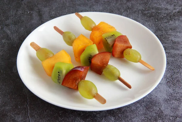 Taze meyvelerden yapılmış çocuk partisi için meyve kebabı. Taze kivi, erik, üzüm, ahşap çubuklarda hurma. Doğum günü partisi için egzotik meyve mezeleri..
