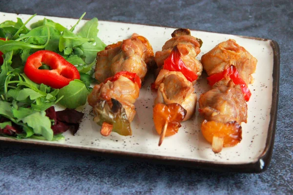 Tabaktaki tahta çubuklarda tavuk budu kebabı. Sıcak meze - kırmızı biberli tavuk şişi ve soğan ve taze sebze salatası.. 