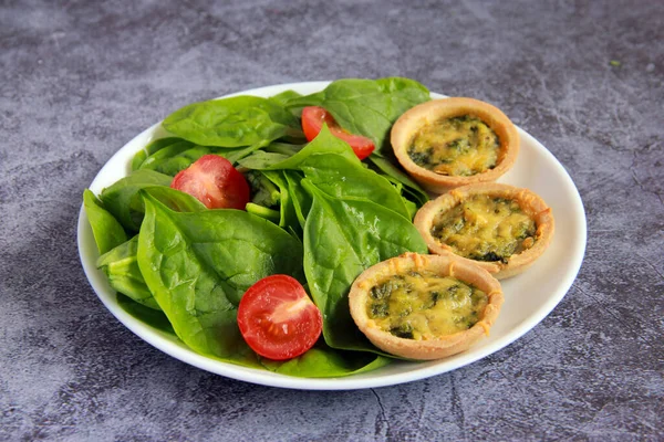 Beyaz tabakta peynirli ve ıspanaklı dört turta. Lezzetli sıcak aperatif - Ispanaklı parmak yiyecekli tartlar ve domates salatası..