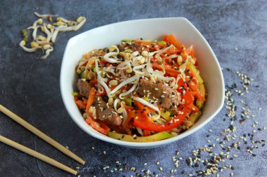 Et, fasulye filizi ve susamlı Asya usulü sebzeler. Çinliler ahşap sopalarla tabakta kızarıyor..