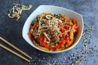 Et, fasulye filizi ve susamlı Asya usulü sebzeler. Çinliler ahşap sopalarla tabakta kızarıyor..