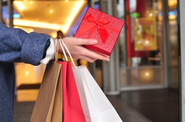 customer's hand holding red and white shopping bags in mall,copy space