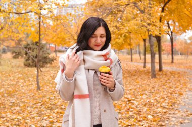 Esmer bir kadının portresi atkı ve palto giymiş kahve içiyor.