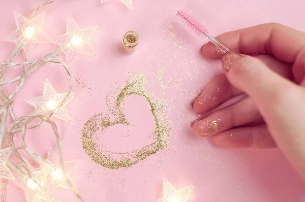 Golden heart from glitter and hand with brush on pink background High quality photo