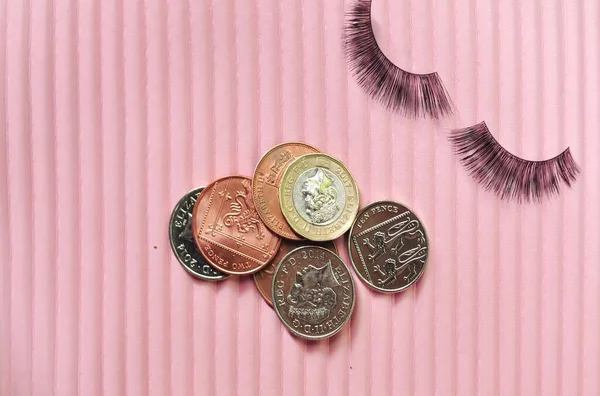 Fake lashes and pounds coins on pink background, price concept. High quality photo