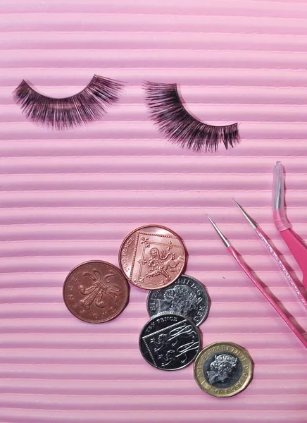 Fake lashes and pounds coins on pink background, price concept. High quality photo