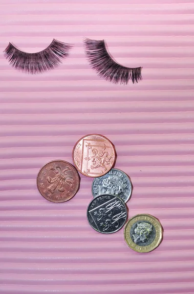 Fake lashes and pounds coins on pink background, price concept. High quality photo