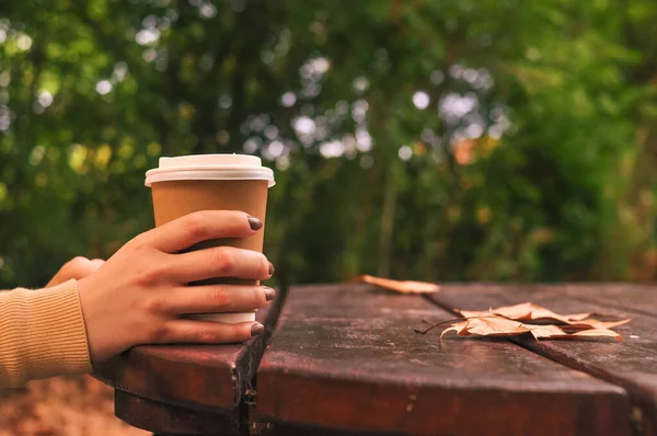 Paper glass of coffee in hand on the orange autumn leaves background . High quality photo