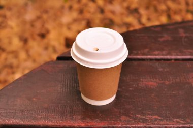 Paper glass of coffee in hand on the orange autumn leaves background . High quality photo