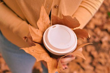 Paper glass of coffee in hand on the orange autumn leaves background . High quality photo