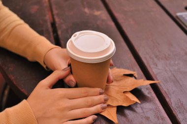 Paper glass of coffee in hand on the orange autumn leaves background . High quality photo