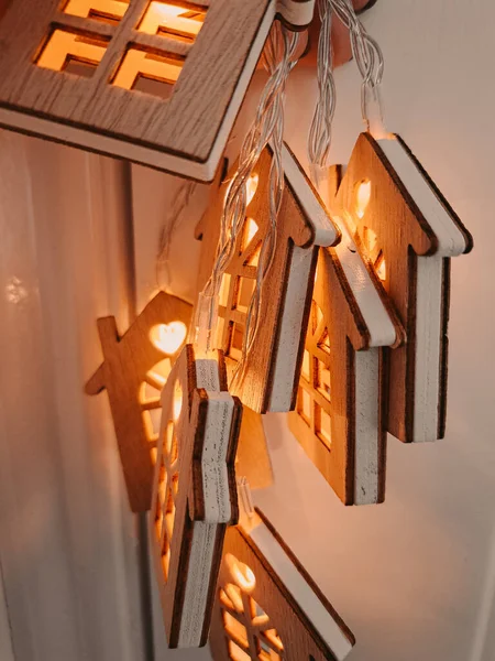 Garland with wooden houses and gold warm light hanging on the wall.