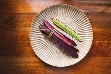 Açık tohumlu bir fasulye kabuğunun yanında tabakta duran bir demet mor Guaje fasulyesi. Oaxaca, Meksika.