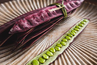 Açık tohumlu bir fasulye kabuğunun yanında tabakta duran bir demet mor Guaje fasulyesi. Oaxaca, Meksika.