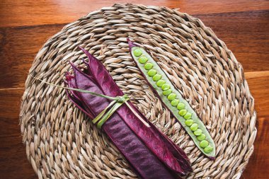 Açık tohumlu bir fasulye kabuğunun yanında tabakta duran bir demet mor Guaje fasulyesi. Oaxaca, Meksika.