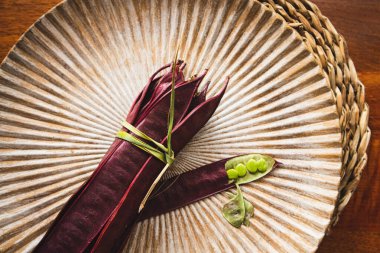 Açık tohumlu bir fasulye kabuğunun yanında tabakta duran bir demet mor Guaje fasulyesi. Oaxaca, Meksika.