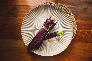 Açık tohumlu bir fasulye kabuğunun yanında tabakta duran bir demet mor Guaje fasulyesi. Oaxaca, Meksika.