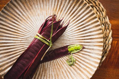 Açık tohumlu bir fasulye kabuğunun yanında tabakta duran bir demet mor Guaje fasulyesi. Oaxaca, Meksika.