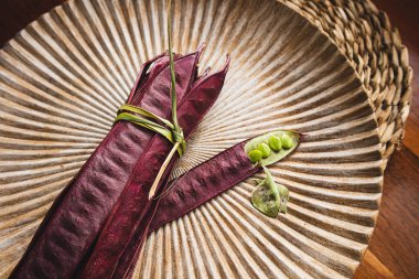 Açık tohumlu bir fasulye kabuğunun yanında tabakta duran bir demet mor Guaje fasulyesi. Oaxaca, Meksika.