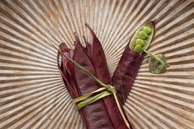 Açık tohumlu bir fasulye kabuğunun yanında tabakta duran bir demet mor Guaje fasulyesi. Oaxaca, Meksika.