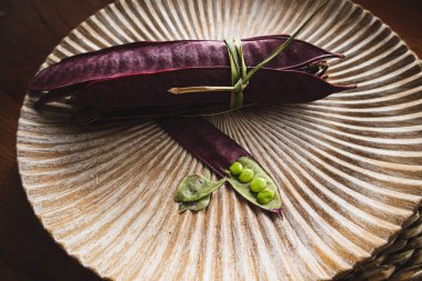 Açık tohumlu bir fasulye kabuğunun yanında tabakta duran bir demet mor Guaje fasulyesi. Oaxaca, Meksika.