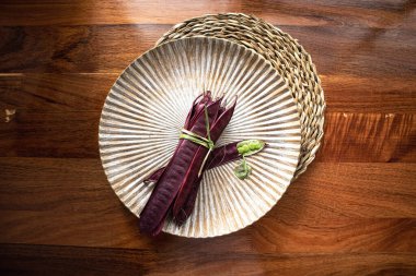 Açık tohumlu bir fasulye kabuğunun yanında tabakta duran bir demet mor Guaje fasulyesi. Oaxaca, Meksika.