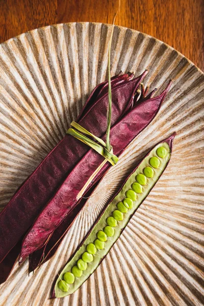 Açık tohumlu bir fasulye kabuğunun yanında tabakta duran bir demet mor Guaje fasulyesi. Oaxaca, Meksika.